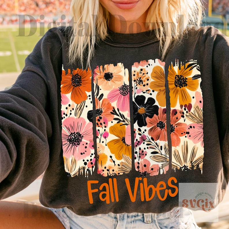 May include: A charcoal gray crewneck sweatshirt featuring a graphic print of three vertical brushstroke panels filled with orange, pink, yellow, and black floral illustrations. The text Fall Vibes is printed in orange below the floral design.
