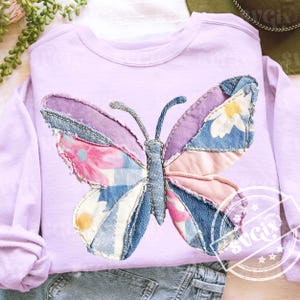 Könnte beinhalten: Ein helllila Sweatshirt mit einem Patchwork-Schmetterlingsdesign. Die Schmetterlingsflügel bestehen aus Jeansstoff und floralen Stoffen in Rosa, Blau und Lila. Das Sweatshirt hat lange Ärmel und einen Rundhalsausschnitt.
