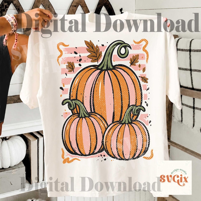 May include: Cream-colored t-shirt featuring a fall-themed graphic. The design includes three pumpkins in shades of orange and pink, with green stems and leaves. The words "Digital Download" are printed on the shirt.