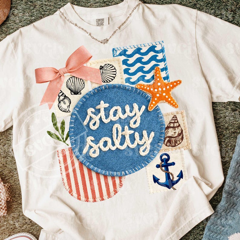 Peut inclure: T-shirt blanc orn&eacute; de motifs marins : coquillages, vagues et &eacute;toile de mer orange. Un &eacute;cusson bleu avec l'inscription "stay salty" en blanc est au centre. Un n&oelig;ud rose et un collier argent&eacute; compl&egrave;tent le design.