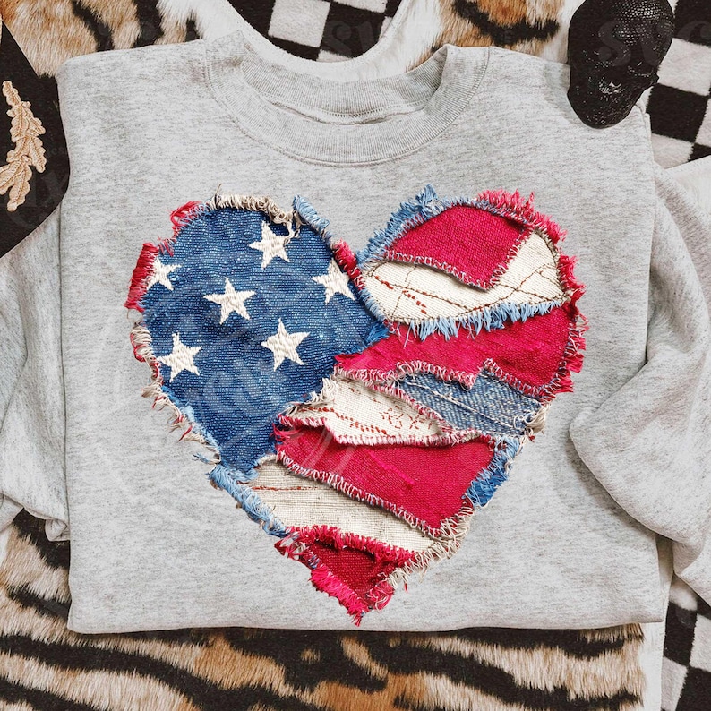 May include: A grey sweatshirt with a heart-shaped patch made from denim and red fabric. The denim section features white stars, similar to the American flag. The edges of the heart are frayed.