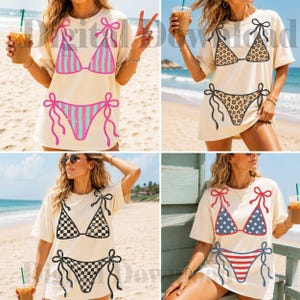 May include: Four cream-colored t-shirts with bikini designs. The designs include pink and blue stripes, leopard print, black and white checkerboard, and a red, white, and blue American flag pattern. The shirts are worn by a person on a beach.