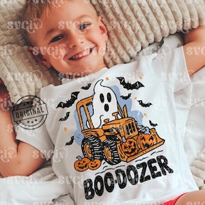 May include: White t-shirt with a Halloween graphic. The design shows a ghost operating an orange bulldozer with jack-o'-lanterns, bats, and the text "BOO DOZER". The shirt has a vintage, distressed appearance.