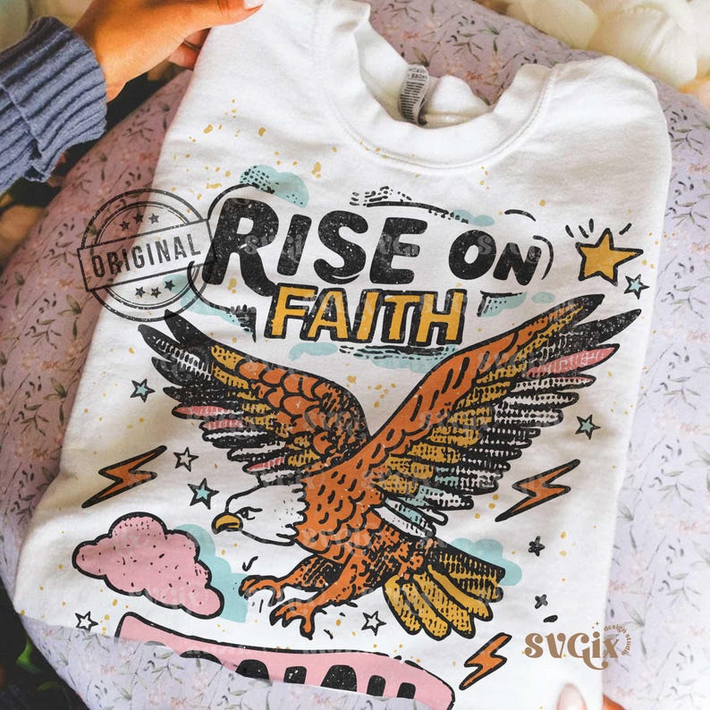 Puede incluir: Sudadera blanca con un gr&aacute;fico de un &aacute;guila con las alas extendidas, las palabras "RISE ON FAITH", estrellas y rayos. La palabra "ORIGINAL" est&aacute; estampada en la parte superior izquierda. La sudadera est&aacute; doblada.