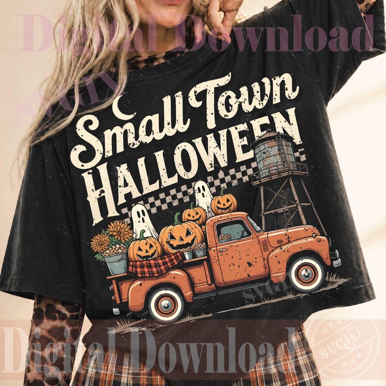 May include: A black t-shirt featuring a graphic print with the text Small Town Halloween. The design includes an orange pickup truck, pumpkins, ghosts, a water tower, and a checkered pattern. The shirt is worn over a leopard print long-sleeve top.