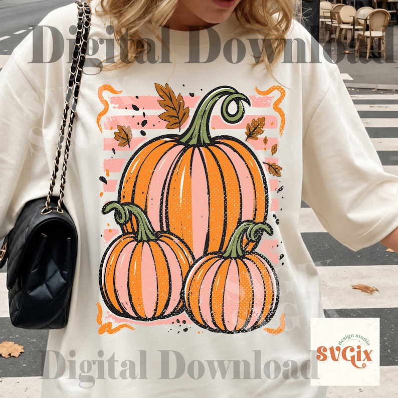 May include: Cream-colored sweatshirt featuring a graphic of three pumpkins in shades of orange and pink, with green stems and leaves. The design includes a pink and white striped background and the text "Digital Download" and "design studio SVGix".