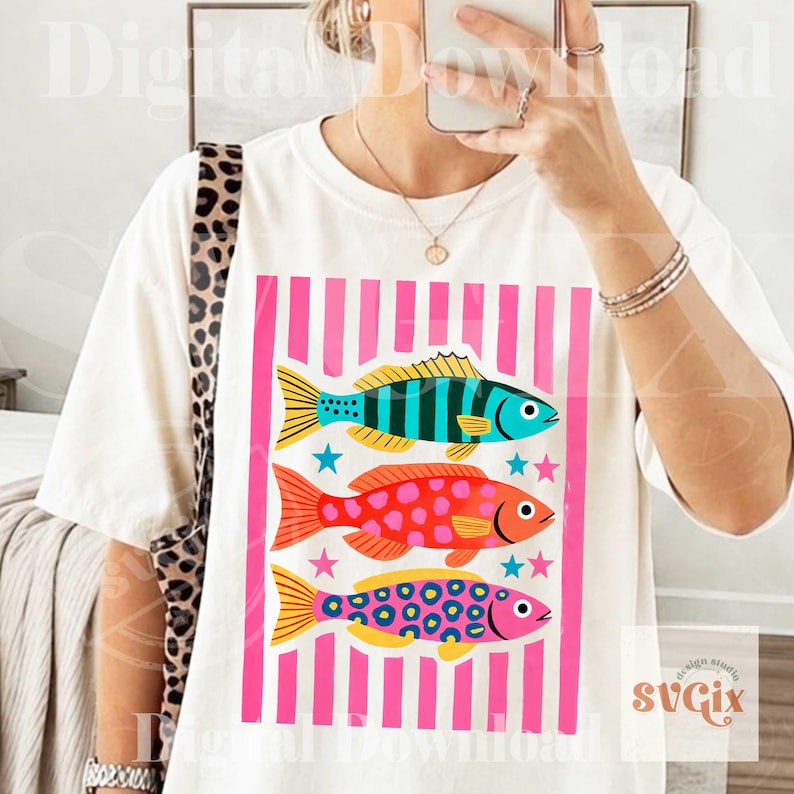 May include: White t-shirt featuring a colorful graphic of three fish with pink and blue accents, set against a pink striped background. The fish have various patterns and colors, including blue stripes, red spots, and pink circles. The text "Digital Download" is visible.