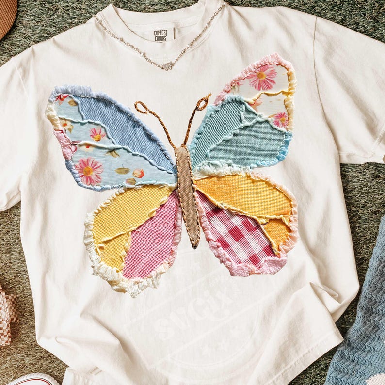 May include: White t-shirt with a colorful patchwork butterfly design. The butterfly wings feature various fabrics in shades of blue, yellow, pink, and floral patterns. The shirt has the text "COMFORT COLORS" on the upper left side.