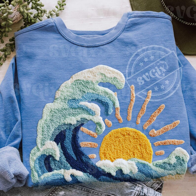 May include: Pale blue sweatshirt with a textured design of a wave and sun. The wave is in shades of blue and white, with a yellow sun and orange rays. The design is centered on the front of the sweatshirt.