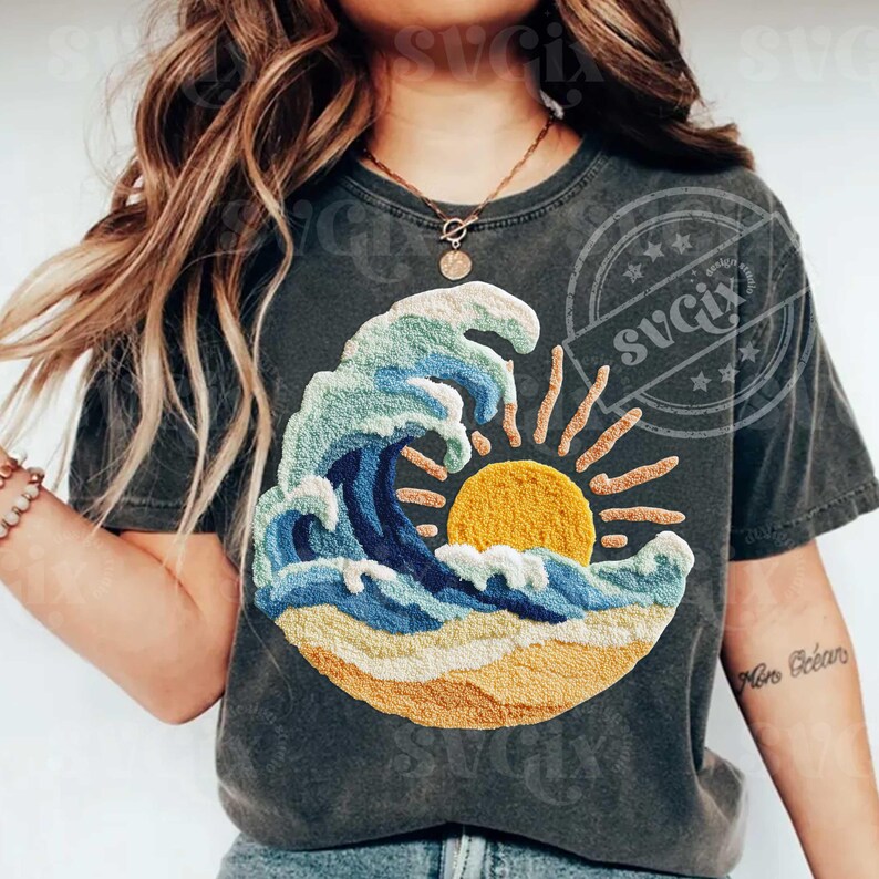 May include: Dark grey t-shirt with an embroidered design of a wave, sun, and beach scene. The wave is in blue and white, with a yellow sun and sandy beach. The shirt has a vintage, worn appearance.