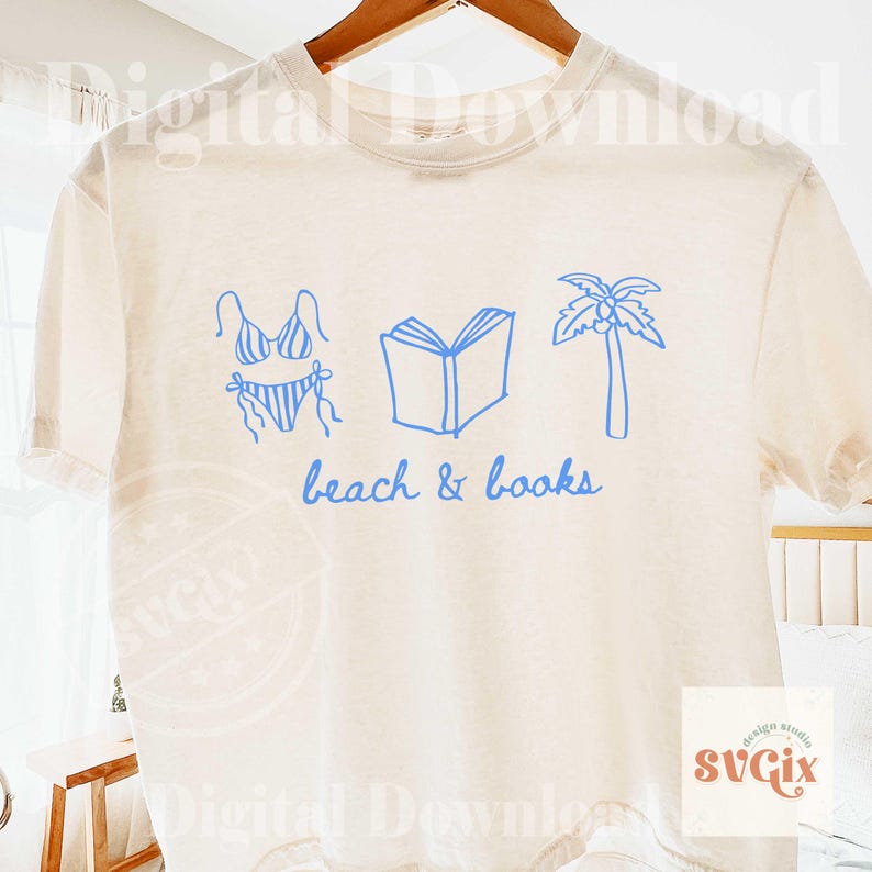 K&ouml;nnte beinhalten: Cremefarbenes T-Shirt mit einer blauen Grafik eines Bikinis, eines offenen Buches und einer Palme. Die Worte "beach & books" sind in blauer Schrift darunter geschrieben. Das Shirt h&auml;ngt an einem Holzb&uuml;gel.