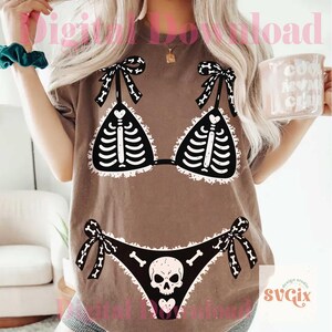 Peut inclure: Un t-shirt marron avec une impression graphique d'un bikini noir pr&eacute;sentant un motif de cage thoracique squelettique blanche sur le haut et un motif de cr&acirc;ne et d'os sur le bas. Le graphisme inclut des bords blancs volant&eacute;s et des liens.