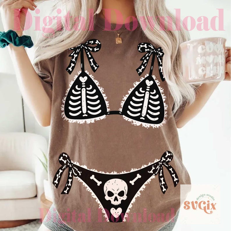 Peut inclure: Un t-shirt marron avec une impression graphique d'un bikini noir pr&eacute;sentant un motif de cage thoracique squelettique blanche sur le haut et un motif de cr&acirc;ne et d'os sur le bas. Le graphisme inclut des bords blancs volant&eacute;s et des liens.