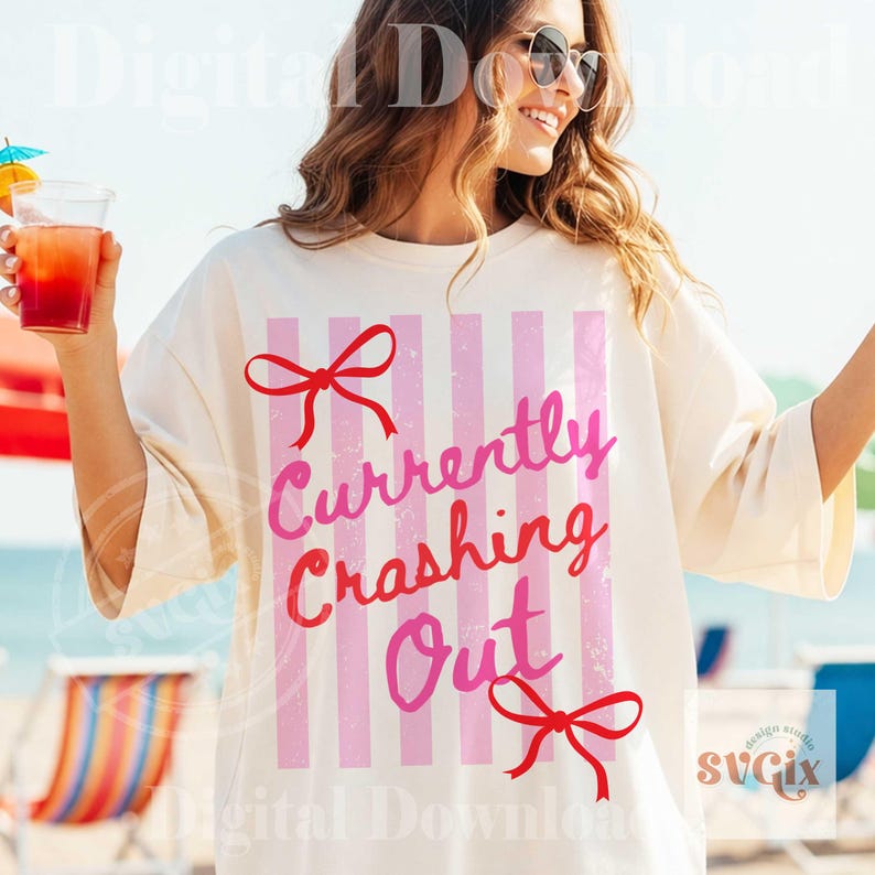 May include: Cream-colored t-shirt with pink vertical stripes and the text "Currently Crashing Out" in pink and red. The shirt features red bow accents and is worn by a person on a beach.