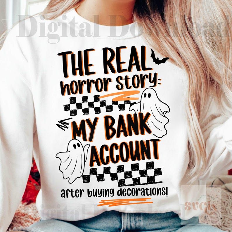 Pode incluir: Camisola branca com o texto "THE REAL horror story: MY BANK ACCOUNT after buying decorations!" em preto e laranja. Apresenta um morcego e duas ilustra&ccedil;&otilde;es de fantasmas, com um padr&atilde;o xadrez.