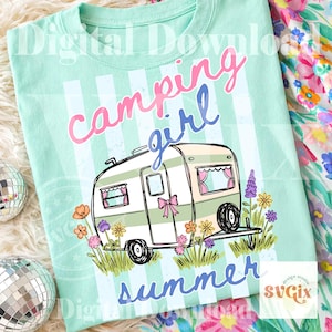 May include: A mint green t-shirt featuring a campervan graphic and the text "camping girl summer." The campervan is white and green with pink details, set against a striped background. Flowers surround the campervan.