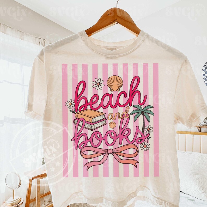 Puede incluir: Camiseta color crema con un dise&ntilde;o de rayas rosas y blancas. La camiseta presenta las palabras "beach and books" en escritura rosa, junto con ilustraciones de una concha, flores, una palmera y una pila de libros.