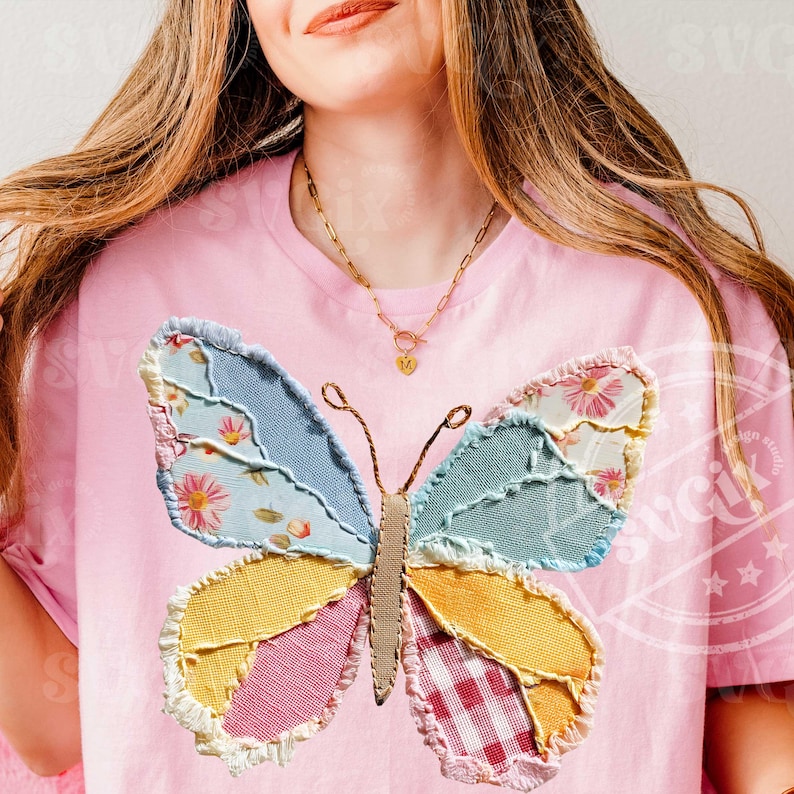 May include: Pink t-shirt featuring a large, patchwork butterfly design. The butterfly has wings in various colors and patterns, including floral, gingham, and solid fabrics. The shirt has a round neckline and short sleeves.