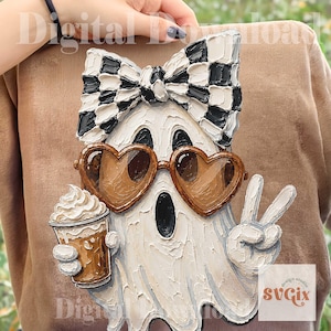 May include: A textured graphic print on a tan shirt featuring a white ghost wearing a black and white checkered bow, brown heart-shaped sunglasses, and holding a coffee cup while making a peace sign. The design has a thick, impasto paint effect.