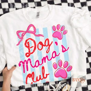 May include: White sweatshirt with the text "Dog Mama's Club" in red and pink script, accented with a pink bow and paw prints. The design features light blue vertical stripes. A casual, comfortable top for dog lovers.