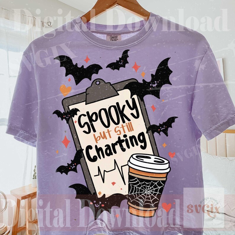 May include: A light purple short-sleeve t-shirt with a graphic print of a clipboard and a coffee cup. The clipboard features the text "Spooky but Still Charting" with a heartbeat line, surrounded by black bats, orange hearts, and stars.