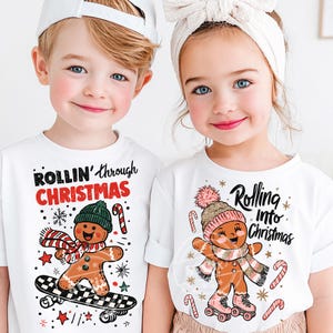 May include: Two children wearing white t-shirts with Christmas graphics. One shirt says "ROLLIN' through CHRISTMAS" with a gingerbread man on a skateboard. The other says "Rolling into Christmas" with a gingerbread man on roller skates.