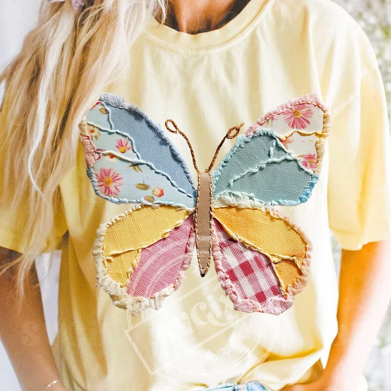 May include: A light yellow t-shirt featuring a large, colorful butterfly applique. The butterfly has wings made of patchwork fabric in shades of blue, yellow, pink, and green, with floral and gingham patterns. The butterfly's body is brown.