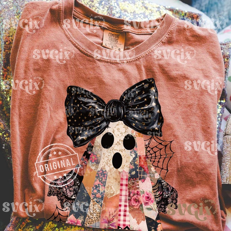 May include: A terracotta-colored t-shirt featuring a ghost design with a black bow and patchwork body. The ghost has three black eye holes and is decorated with a spiderweb. The word "ORIGINAL" is stamped on the shirt.