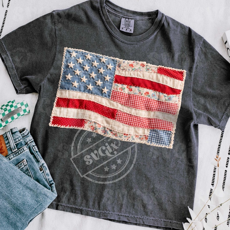 Pu&ograve; includere: T-shirt grigio scuro con un design a patchwork della bandiera americana. La bandiera presenta tessuto blu, rosso e bianco con stelle e strisce. La maglietta &egrave; abbinata a jeans blu e un fermaglio per capelli a scacchi verdi e bianchi.