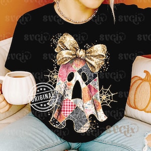 Op de afbeelding: Zwart T-shirt met een patchwork spookontwerp en een gouden glitterstrik. De geest heeft bloemen- en spinnenwebpatronen. Het woord "ORIGINAL" is linksonder in de afbeelding gestempeld.
