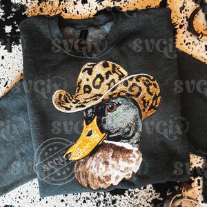 May include: Dark gray sweatshirt featuring a rhinestone-studded duck wearing a leopard print cowboy hat. The duck has a yellow beak and is embellished with rhinestones. The design is centered on the front of the sweatshirt.