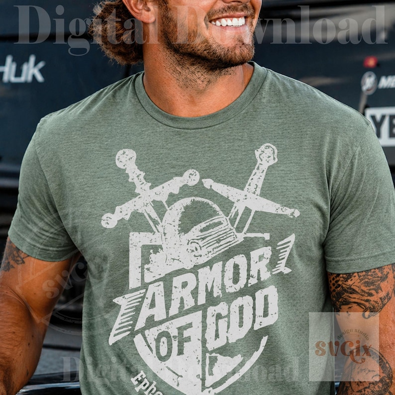 K&ouml;nnte beinhalten: Gr&uuml;nes T-Shirt mit einem wei&szlig;en, verblassten Grafikdesign. Das Design zeigt einen Helm, gekreuzte Schwerter und den Text "ARMOR OF GOD" in einem Schild. Das Wort "Epheser" ist am unteren Rand des Schildes aufgedruckt.