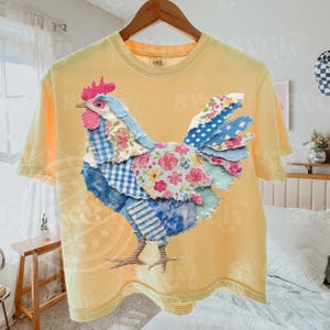 May include: Yellow t-shirt featuring a patchwork rooster design. The rooster is made of various patterned fabrics, including floral, gingham, and polka dots, in shades of blue, pink, and white. The shirt has a crew neck and short sleeves.