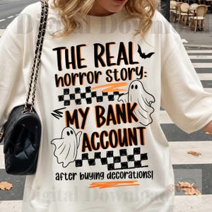 Pode incluir: Camiseta de manga comprida creme com o texto "THE REAL horror story: MY BANK ACCOUNT after buying decorations!" em preto e laranja. Apresenta gr&aacute;ficos de fantasmas e morcegos, perfeita para o Halloween.