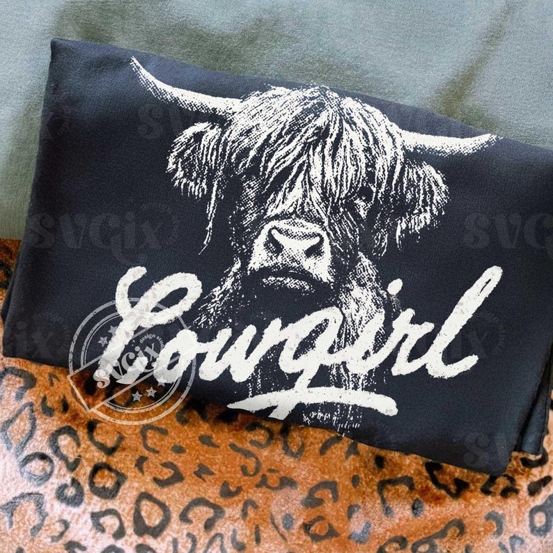 May include: Black pillow with a white graphic of a Highland cow's face and the word "Cowgirl" in a script font. The pillow is on a leopard print surface.