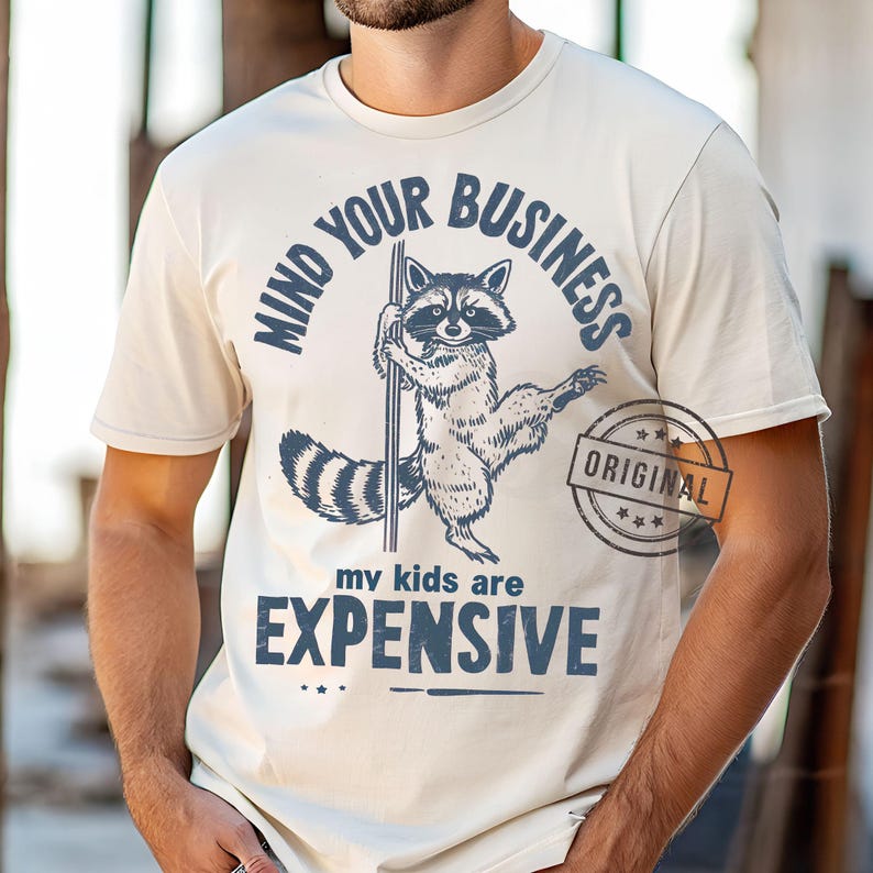 Pu&ograve; includere: T-shirt color crema con un procione che tiene un palo, con la scritta "MIND YOUR BUSINESS" sopra e "my kids are EXPENSIVE" sotto. &Egrave; presente anche un timbro con la scritta "ORIGINAL".