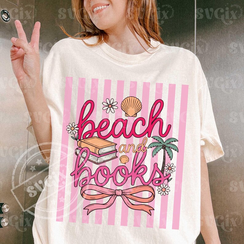 May include: Cream-colored t-shirt featuring a pink and white striped design with the words "beach and books" in pink script. The graphic includes illustrations of books, seashells, flowers, a palm tree, and a bow.