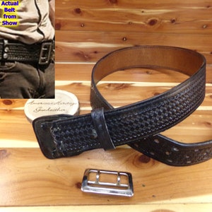 Puede incluir: Un cinturón de cuero negro con patrón de tejido de cesta, una trabilla de cuero y una hebilla rectangular de metal plateado por separado. El cinturón se muestra en una vista principal y una inserción con el texto Actual Belt from Show.