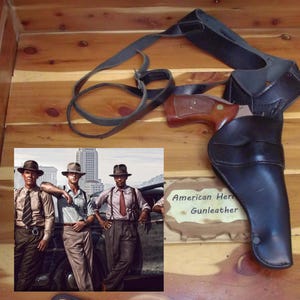 May include: A black leather shoulder holster with a brown wood-handled revolver, accompanied by a photograph of three men in 1940s attire and a wooden sign reading American Heritage Gunleather, all displayed on a polished wood surface.