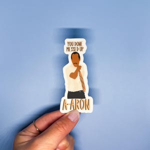 May include: A sticker featuring a cartoon illustration of a man with a brown complexion, wearing a white shirt and a brown tie. The man is holding his hands up in a gesture of exasperation. The sticker has the text "You done messed up" above the man and "A-aron" below him.
