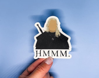 May include: A white sticker with a black and white illustration of a character from a fantasy series. The character is wearing a black shirt and has long white hair. The text "Hmmmm." is printed below the character.
