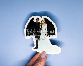 May include: A sticker featuring a couple with a black and white silhouette of a dragon behind them. The text reads "To stars who listen and the dreams that are answered."