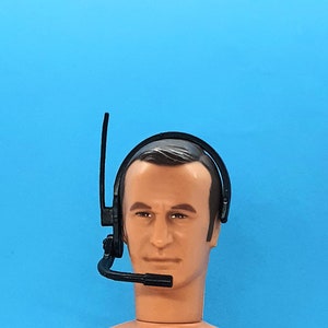 May include: A black headset with a boom microphone. The headset is being worn by a person with brown hair and a light brown complexion.