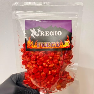 May include: A clear plastic bag filled with red corn snacks. The bag has a purple label with the word "REGIO" and "FUEGO" in yellow and orange flames. The snacks appear to be coated in a red seasoning.