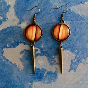 May include: A pair of dangle earrings with a round, orange and white striped cabochon and a long, pointed bronze pendant.