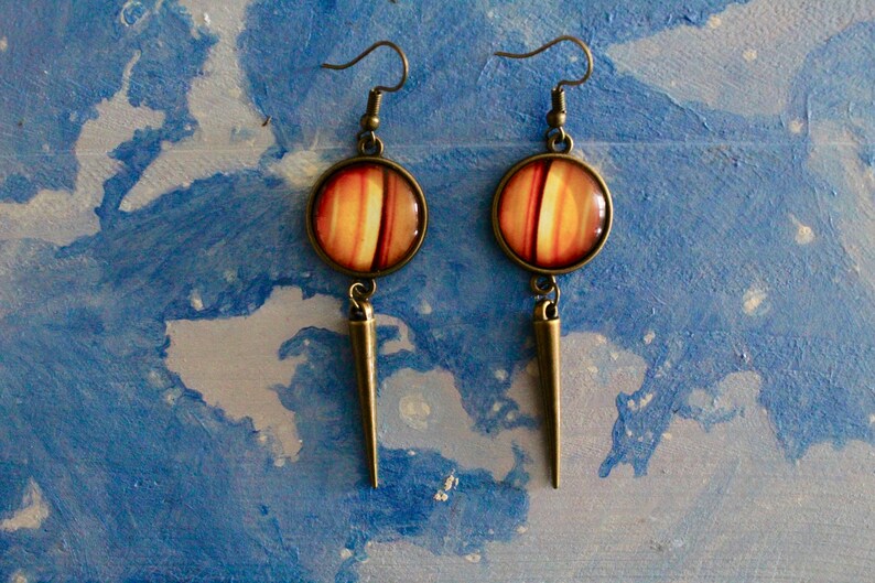 May include: A pair of dangle earrings with a round, orange and white striped cabochon and a long, pointed bronze pendant.