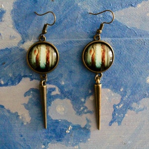 May include: A pair of long, bronze earrings with a round, colorful glass pendant. The pendant features a swirling pattern of blue, white, and brown.