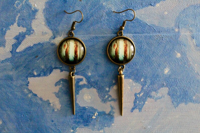 May include: A pair of long, bronze earrings with a round, colorful glass pendant. The pendant features a swirling pattern of blue, white, and brown.