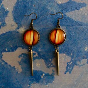 May include: A pair of dangle earrings with a round, orange and brown striped glass charm and a long, pointed bronze pendant.