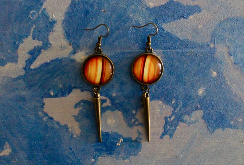 May include: A pair of dangle earrings with a round, orange and brown striped glass charm and a long, pointed bronze pendant.